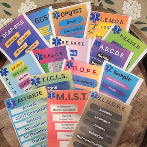 Puede incluir: Una colección de tarjetas de referencia médica coloridas con varios acrónimos y términos como DCAP-BTLS, OPQRST y SLUDGE. Las tarjetas están dispuestas sobre una superficie de madera, con información de servicios médicos de emergencia.