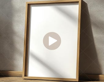 May include: A wooden frame with a white background and a play button icon in the center. The frame is sitting on a wooden floor with a light gray wall in the background. VIDEO ART MOCKUP is written in black text at the bottom of the image.