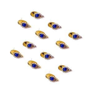 May include: A collection of twelve teardrop-shaped stud earrings featuring a gold-tone metal setting. Each earring is accented with a central peacock feather pattern in shades of blue and brown, surrounded by a border of small clear rhinestones.