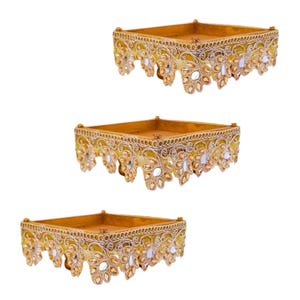May include: Three gold-colored decorative trays with ornate, scalloped edges. Each tray has a square shape with a raised rim and is embellished with clear and amber-colored gemstones. The trays are arranged on a white background.
