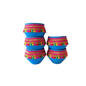 May include: A stack of six turquoise blue ceramic pots. Each pot is adorned with a pink and gold trim, and colorful tassels. The pots are arranged in a visually appealing, stacked configuration, showcasing their decorative design.