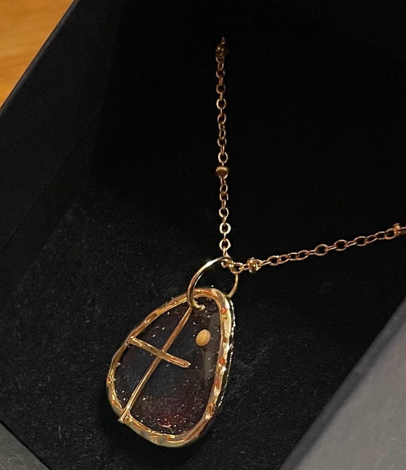 Peut inclure: Un collier dor&eacute; avec un pendentif en forme de goutte contenant un int&eacute;rieur sombre et paillet&eacute;. Le pendentif est entour&eacute; d'un cadre en m&eacute;tal dor&eacute;, incluant une fine barre transversale dor&eacute;e et un petit accent circulaire dor&eacute;, sur une cha&icirc;ne.