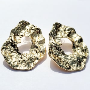 May include: A pair of gold-toned earrings with a textured, irregular, circular shape. The earrings have a large hole in the center.