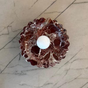 Può includere: Una palla di marmo bianco che riposa in una ciotola di marmo rosso e bianco con bordo smerlato.
