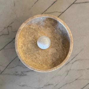 May include: A round, beige, marble bowl with a white, round, smooth object in the center.