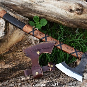 May include: A hand-forged Viking axe with a wooden handle wrapped in black leather. The handle is decorated with a braided pattern and runes. The axe head is made of steel and has a sharp edge. The axe comes with a brown leather sheath.