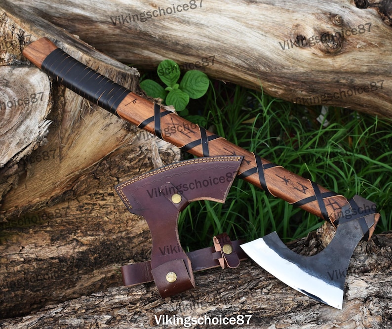May include: A hand-forged Viking axe with a wooden handle wrapped in black leather. The handle is decorated with a braided pattern and runes. The axe head is made of steel and has a sharp edge. The axe comes with a brown leather sheath.