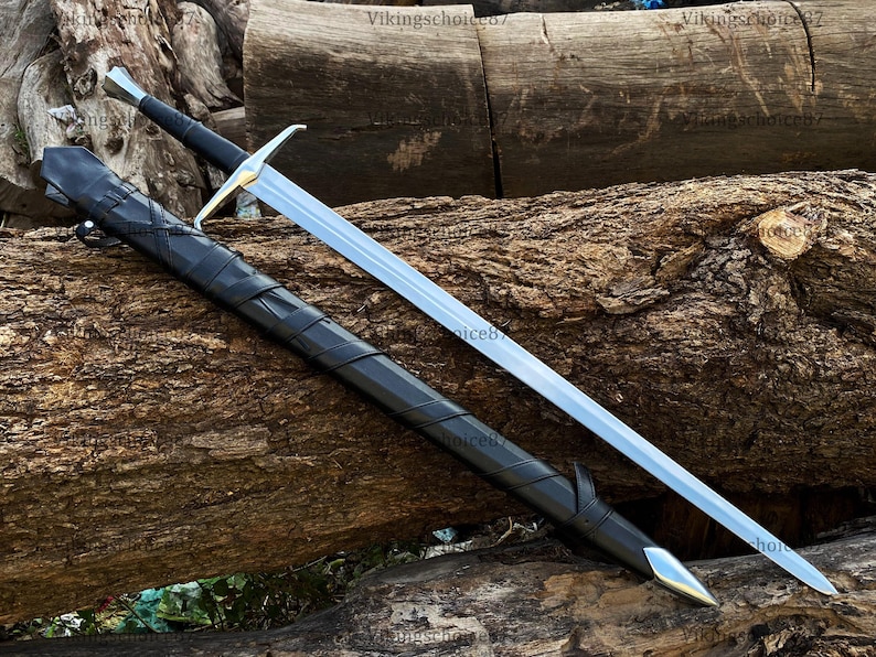 May include: A long, silver sword with a gold crossguard and black handle rests beside its black leather sheath. The sword and sheath are displayed on a textured, brown log, showcasing a medieval or fantasy theme.