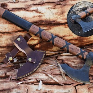 May include: A black and brown Viking axe with a leather handle and a leather sheath. The axe has a curved blade and is decorated with runes.
