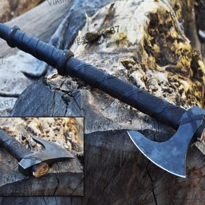 May include: A black axe with a curved blade and a wooden handle wrapped in dark leather. The axe head is a dark gray color. The handle has a textured pattern. A smaller inset image of the axe is in the lower left corner.