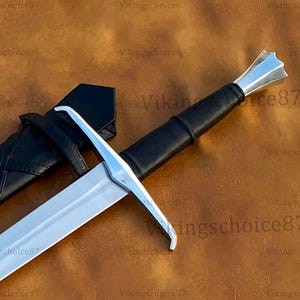 May include: A silver and black sword with a leather-wrapped handle and a black sheath. The sword has a double-edged blade and a crossguard. The handle is black and the sheath is also black. The sword is a historical or fantasy item.