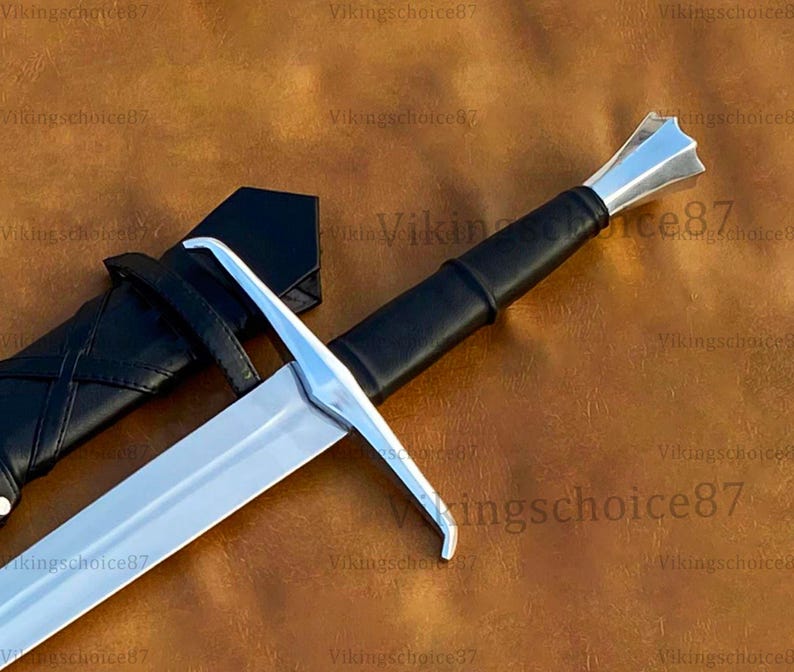 May include: A silver and black sword with a leather-wrapped handle and a black sheath. The sword has a double-edged blade and a crossguard. The handle is black and the sheath is also black. The sword is a historical or fantasy item.