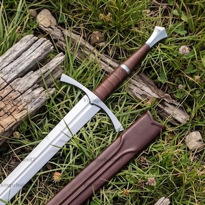 May include: A steel sword with a double-edged blade, a silver crossguard, and a brown leather-wrapped grip featuring a silver pommel. The sword is accompanied by a matching brown leather scabbard with a contoured opening.