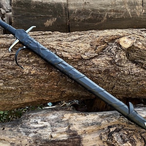 May include: A long, black sword with a silver blade and crossguard, sheathed in a matching black scabbard. The sword rests on a weathered, brown log, showcasing its length and design. A leather strap is attached to the scabbard.