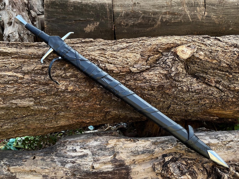 May include: A long, black sword with a silver blade and crossguard, sheathed in a matching black scabbard. The sword rests on a weathered, brown log, showcasing its length and design. A leather strap is attached to the scabbard.