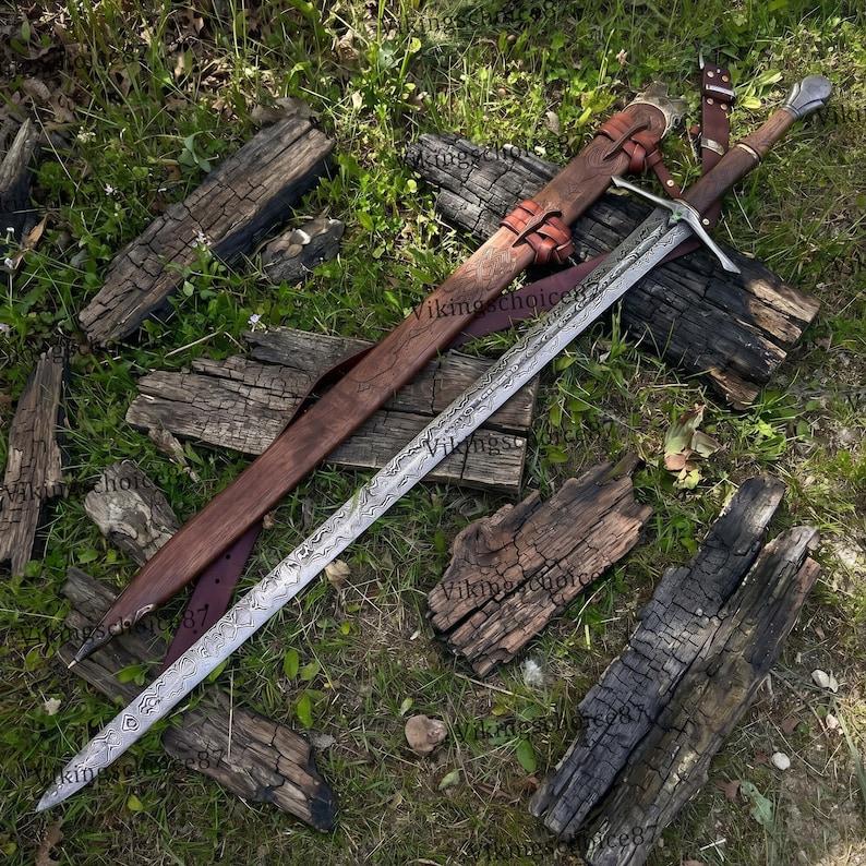 May include: A long, ornate sword with a patterned blade and a wooden handle, resting on weathered wood and grass. The sword has a leather sheath and straps, suggesting a historical or fantasy theme.