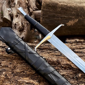 Pode incluir: Uma espada medieval com uma lâmina prateada e um cabo preto, repousando sobre uma superfície de madeira. A espada tem uma guarda dourada e é acompanhada por uma bainha de couro preta. O design sugere um tema histórico ou de fantasia.