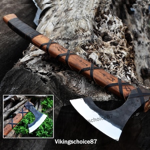 May include: A Viking axe with a wooden handle wrapped in black leather and a steel head. The handle is decorated with runes and the head is polished to a shine.