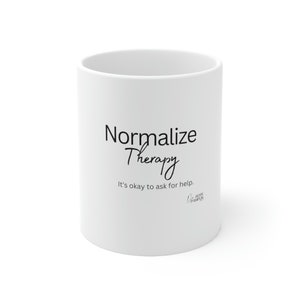 Könnte beinhalten: Weißer Keramikbecher mit dem schwarzen Schriftzug "Normalize Therapy" und dem Satz "It's okay to ask for help." Der Becher hat auch das Hope Pampus Logo. Schlichtes Design.