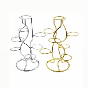 May include: Two decorative metal stands, one silver and one gold, are displayed. Each stand has a circular base, a central stem, and several circular platforms at different heights. The stands are designed to hold small items.