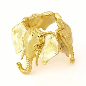 May include: A gold-colored ring featuring an elephant design. The ring is crafted with intricate details, showcasing the elephant's head, trunk, and ears. The ring is a statement piece, perfect for animal lovers.