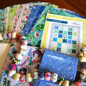 May include: A quilting kit with a variety of blue, green, and pink patterned fabrics, a white backing fabric, a blue fabric with white stars, and a printed pattern for a quilt called "Pixie Squared" by Riley Blake Designs.