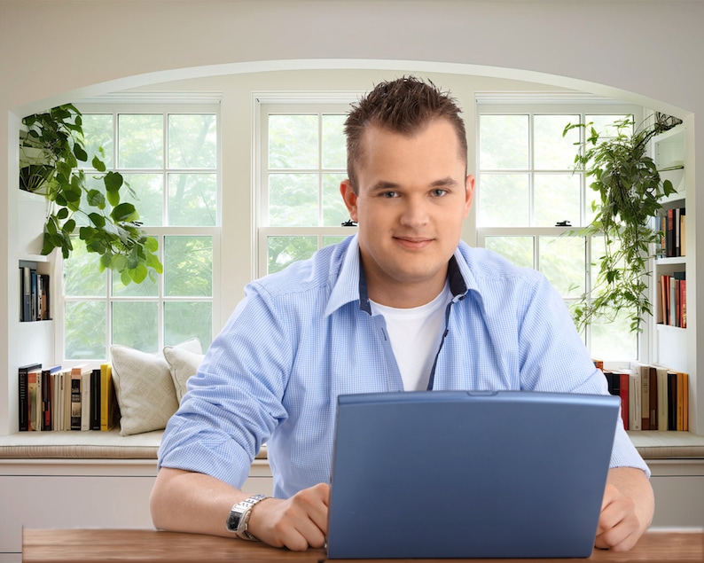 Virtual background of man sitting at desk containing laptop and in front of window seat with bookshelf for zoom and virtual meeting streaming backdrop.