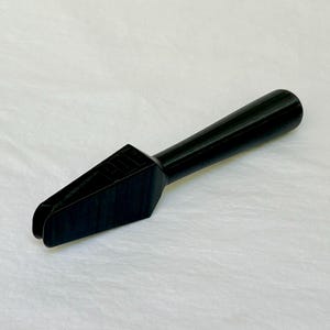 May include: A black, 3D-printed tool with a handle and a forked end. The tool has a geometric design on the head. The handle is cylindrical, and the forked end has a U-shaped opening. The tool is likely used for a specific task.