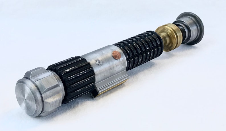 May include: A disassembled lightsaber with a silver and black handle, a brass connector, and a silver emitter. The lightsaber is on a white surface.