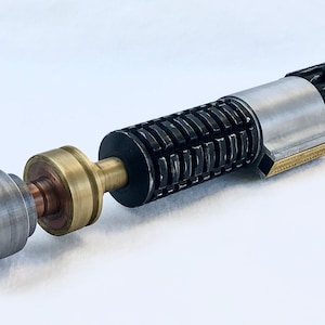 May include: A disassembled lightsaber with a black and silver handle, a gold and copper connector, and a silver emitter. The lightsaber is on a white surface.