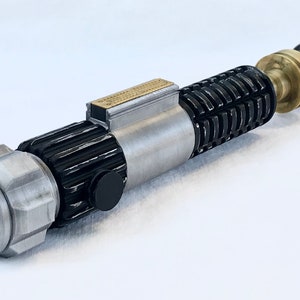 May include: A silver and black lightsaber prop with a brass accent. The lightsaber is made of metal and has a textured surface.