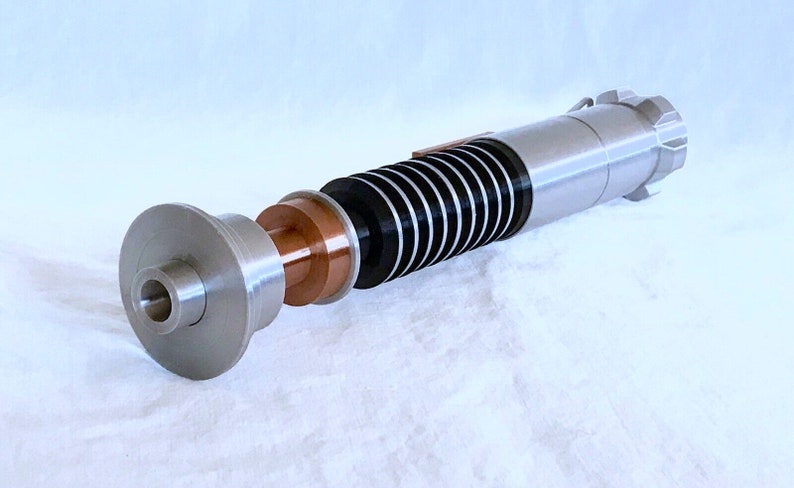 May include: A disassembled lightsaber with a silver and black handle, a copper coloured emitter, and a silver and black blade.