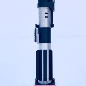 May include: A black and silver lightsaber replica with a black stand. The stand has a red label that reads "DARTH VADER".