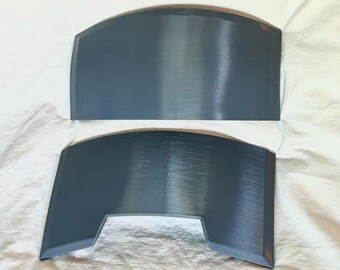 May include: Two gray, curved, shield-shaped objects. The top object has a rounded top edge. The bottom object has a similar shape, but with a rectangular cutout at the bottom. Both objects have a brushed metal appearance.