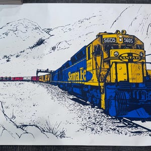 May include: A vintage poster featuring a blue and yellow Santa Fe train engine with the number 5605 on the side. The train is traveling through a mountainous landscape.