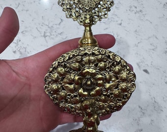 May include: Ornate antique perfume bottle with a gold finish. The bottle features intricate floral and cherub designs, with a decorative filigree top. The base is round and detailed, adding to its vintage charm.