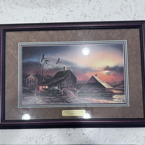 May include: Framed artwork depicting a rural landscape at dusk. The scene includes a house, barn, and a truck, with geese flying overhead. The sky transitions from dark blue to orange, with the text "PREPARED FOR THE SEASON" and the artist's name.