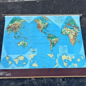 May include: A vintage world map on a blue background, with continents in shades of brown and green. The map includes the text "MAP OF THE WORLD" and "THE WORLD". It is mounted on a metal rod with a brown bottom.