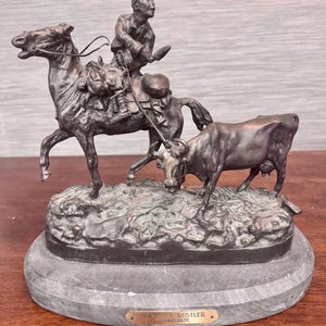 May include: Bronze sculpture of a cowboy on horseback, herding a cow. The sculpture is on a marble base and has a plaque that reads "Lone Star Rustler by Grechov".