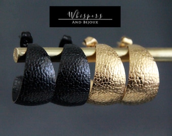 May include: Three pairs of hoop earrings, one black, one black, and two gold. The earrings have a textured, hammered finish.