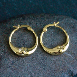 Peut inclure: Une paire de boucles d'oreilles créoles en or avec un motif de croissant de lune et un petit accent de pierre claire.