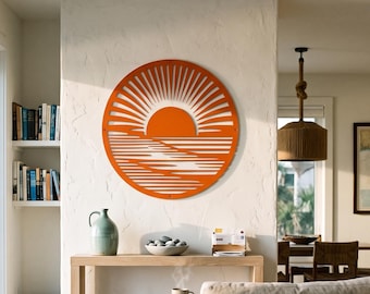 May include: A circular orange metal wall art piece featuring a cut-out design of a sun rising over a horizon with radiating sunbeams above and horizontal lines representing water below, mounted on a white textured wall above a wooden console table.