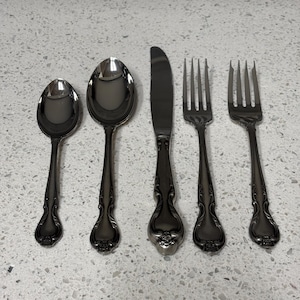 May include: A set of five silver-plated cutlery pieces, including a knife, two forks, and two spoons. The cutlery has an ornate design with a floral pattern.