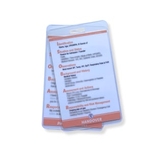 Peut inclure: Deux porte-cartes en plastique transparent avec du texte blanc et orange. Les cartes contiennent des informations médicales, notamment "Identification", "Observations" et "Assessment and Actions". Le mot "HANDOVER" est visible en bas.