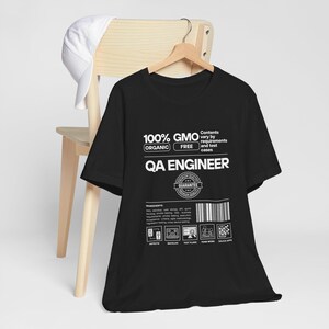 May include: Black t-shirt with white text that reads "100% GMO FREE ORGANIC QA ENGINEER" with a white circle containing the word "GUARANTEE".