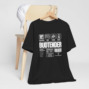 May include: Black t-shirt with white text that reads "Budtender" and a graphic of a dispensary, card, flower, and CBD oil. The text below reads "Content Description: Unrestricted, Creating Positive Customer Experiences, It's Also Somewhere".