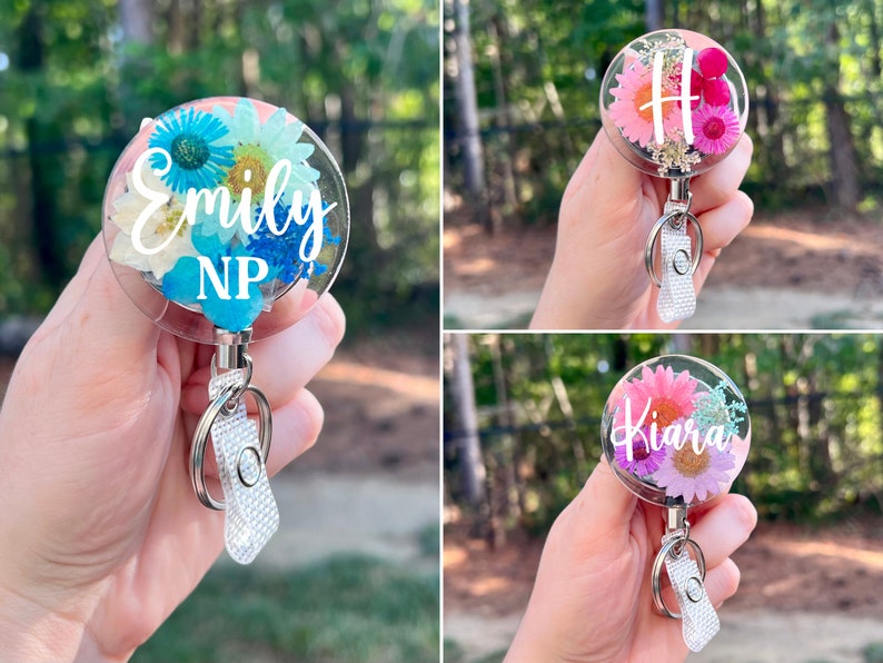 May include: Clear, round badge reels with floral designs and personalized text. One reel features blue and white flowers with "Emily NP". Another has pink flowers and the letter "H". The third has pink flowers and "Kiara".