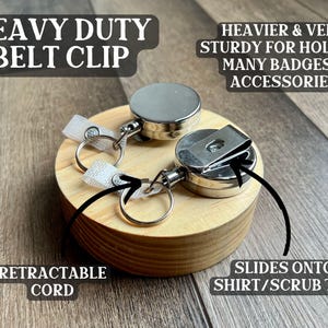 May include: A heavy-duty belt clip with a retractable cord. The clip is made of silver metal and has a sturdy design for holding badges and accessories. It slides onto a shirt or scrub top. The text on the image says "Heavy Duty Belt Clip".