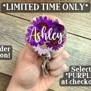 May include: A clear, round badge reel with purple flowers and the name "Ashley" in white script. The text "*LIMITED TIME ONLY*", "Order Soon!", and "Select *PURPLE* at checkout!" are also visible.