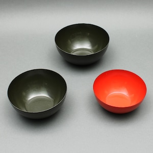 Puede incluir: Tres cuencos pequeños y redondos. Dos son de color verde oscuro y uno rojo brillante. Los cuencos tienen un acabado liso y brillante y están vacíos. Los cuencos están colocados sobre una superficie gris.